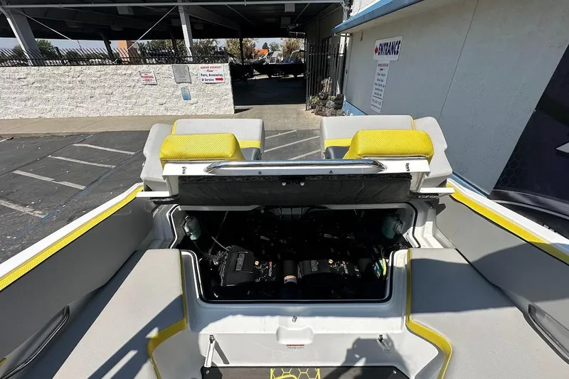 Slide: The Image of 2023 Scarab 215 ID boat engine compartment with yellow-accented seating in a parking area. - 27