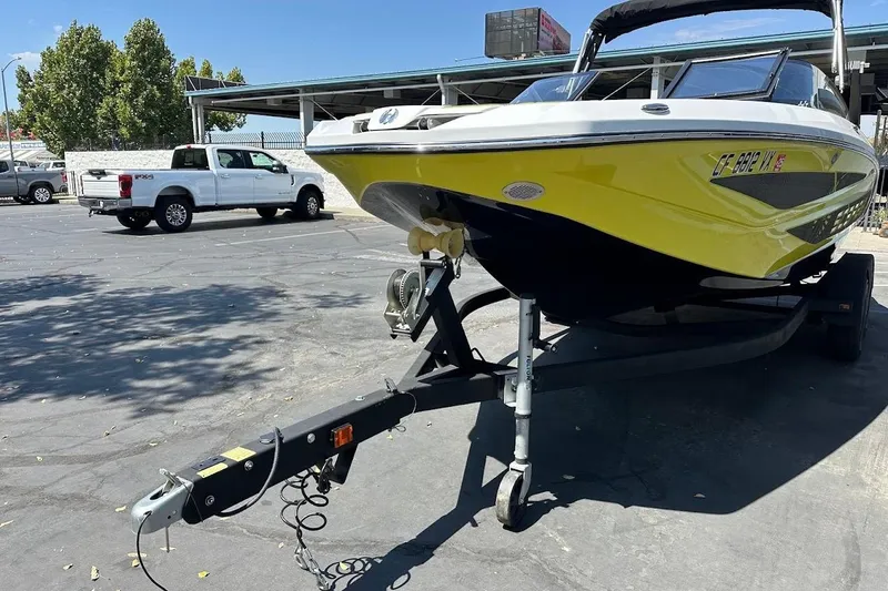 Slide: The Image of 2023 Scarab 215 ID boat on trailer in parking lot, yellow hull, sunny day. - 4