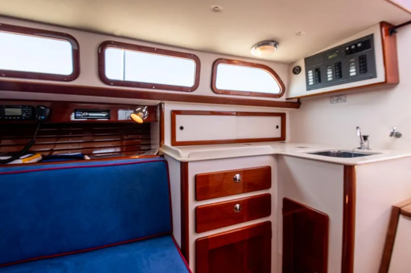 Slide: The Image of Interior of 2006 Morris M36 Daysailer with blue seating, wooden cabinetry, and compact kitchenette. - 33