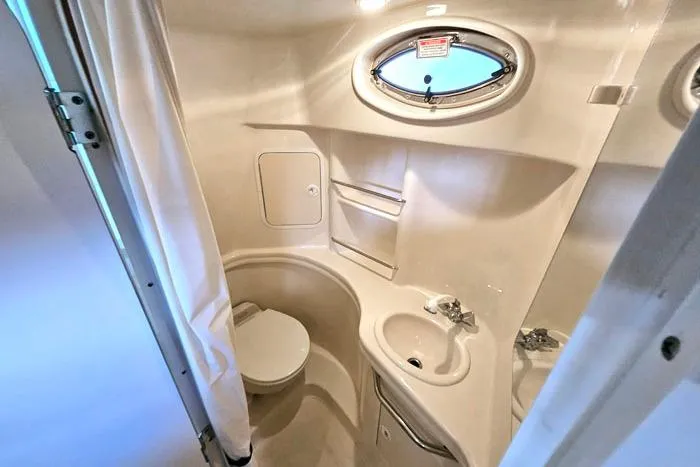 Slide: The Image of 2004 Sea Ray 300 Sundancer bathroom with toilet, sink, and porthole window. - 21