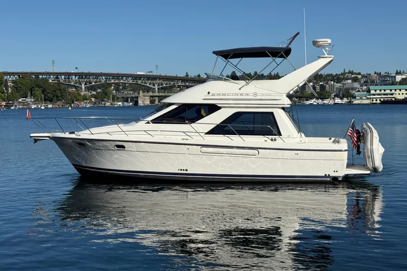 Slide: The Image of 1999 Bayliner 3788 Command Bridge Motoryacht on calm water, with cityscape and bridge in background. - 10