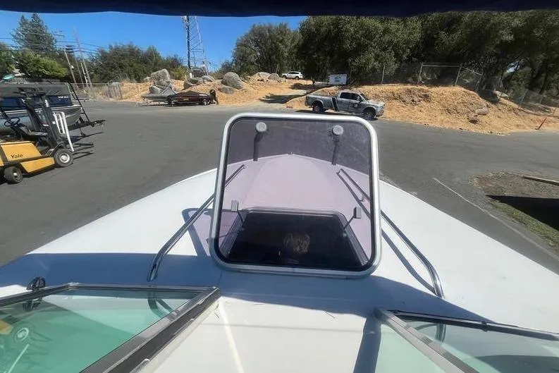 Slide: The Image of 1997 Reinell 240 boat parked outdoors, surrounded by vehicles and trees. - 26