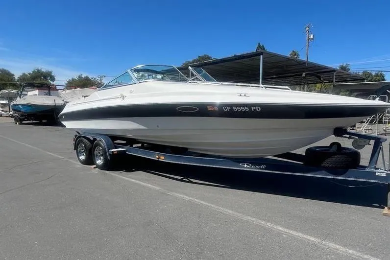 Slide: The Image of 1997 Reinell 240 boat on trailer, parked outdoors under clear blue sky. - 3