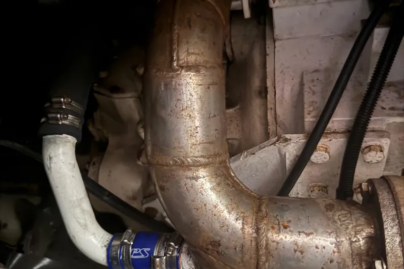 Slide: The Image of Engine components of a 1974 Pacemaker 48 Sportfisherman boat, featuring metal pipes and hoses. - 37