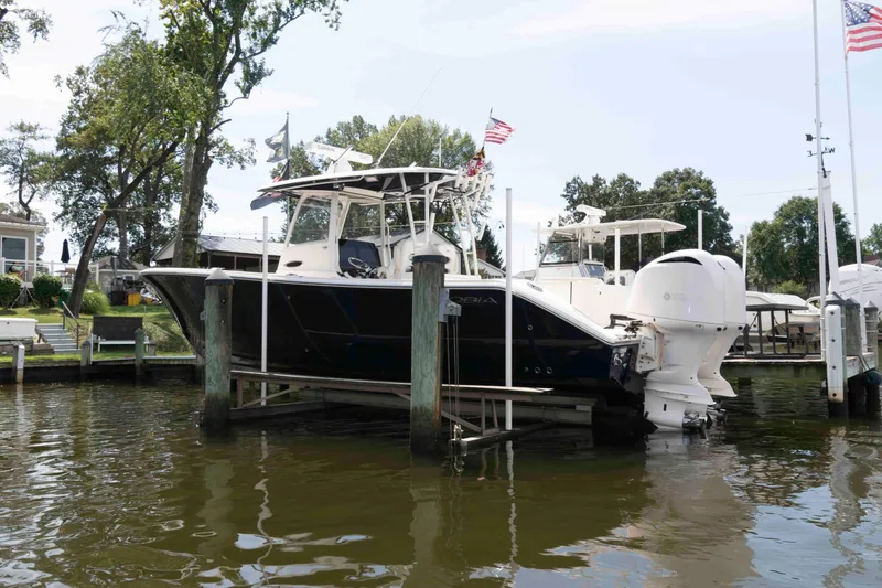 Slide: The Image of 2020 Cobia 320 Center Console boat docked on a lift by the water. - 3