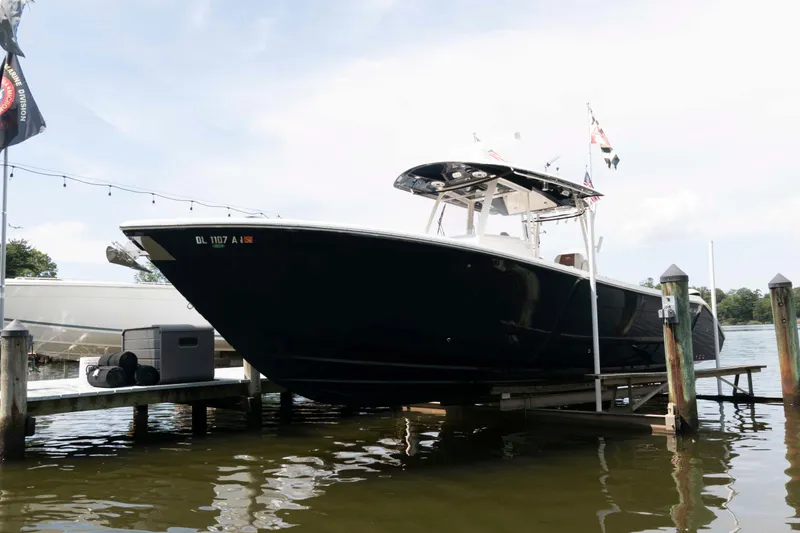 Slide: The Image of 2020 Cobia 320 Center Console boat docked with twin engines, surrounded by trees and flags. - 4