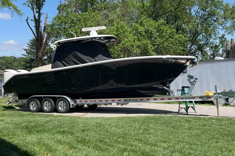 Slide: The Image of 2020 Cobia 320 Center Console boat docked by a serene lake under a cloudy sky. - 6