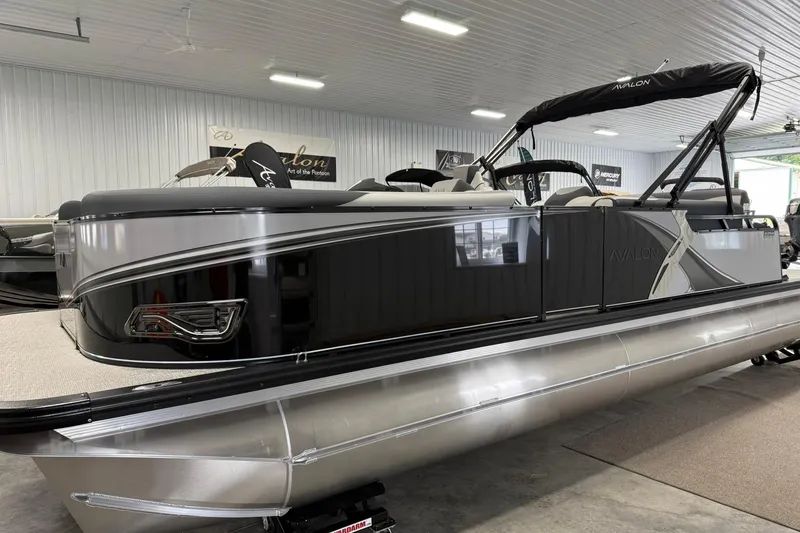 Slide: The Image of 2025 Avalon LSZ Cruise Rear Bench pontoon boat in showroom, sleek design, black and silver finish. - 4