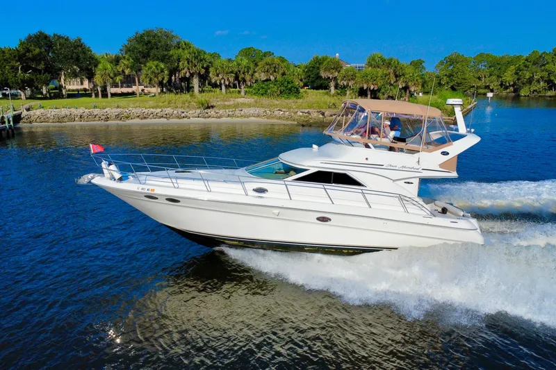The Image of 2003 Sea Ray 400 Sedan Bridge cruising on a sunny day near a lush shoreline. - 0