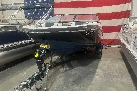 Slide: The Image of 2023 Yamaha Boats SX195 on trailer, displayed indoors with American flag backdrop. - 0