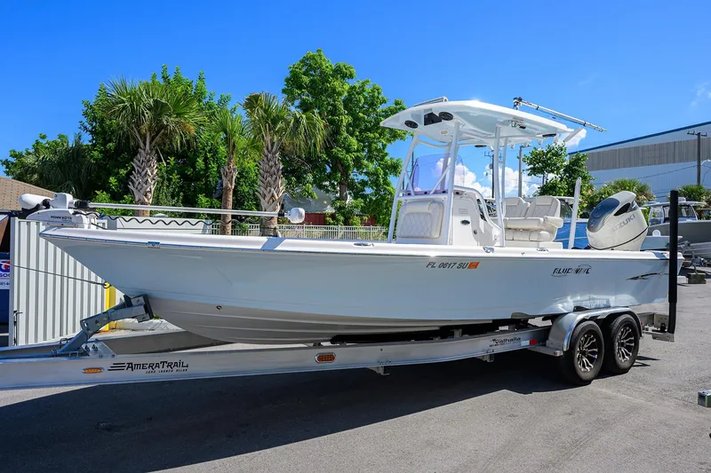 Slide: The Image of 2021 Blue Wave 2600 PureBay boat on trailer, surrounded by palm trees and clear blue sky. - 0