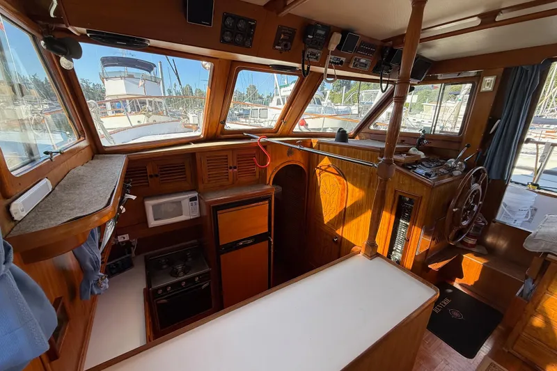 Slide: The Image of 1983 CHB 41 Classic Trawler interior with wooden helm, kitchen, and marina view. - 14