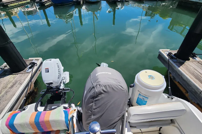 Slide: The Image of Boston Whaler 21 Conquest boat docked, featuring Suzuki outboard motor, colorful towel, and clear water reflection. - 18