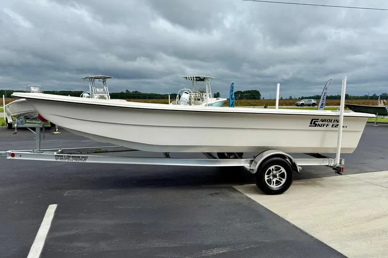 Slide: The Image of 2026 Carolina Skiff E21 DLX Kit Boat on trailer, parked outdoors under cloudy sky. - 5