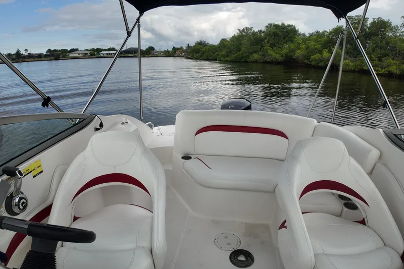 Slide: The Image of 2015 Hurricane SunDeck 2200 OB boat interior with white and red seating on a calm lake. - 17