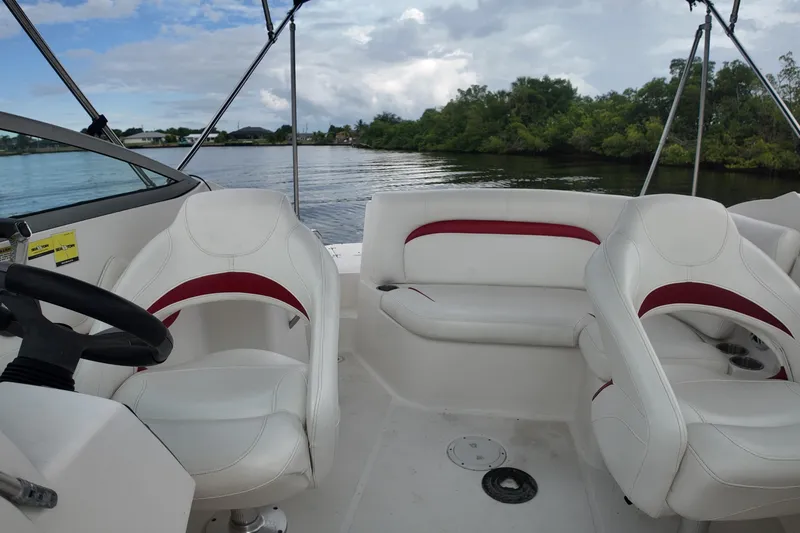 Slide: The Image of 2015 Hurricane SunDeck 2200 OB boat interior with white and red seating, on a calm lake. - 18