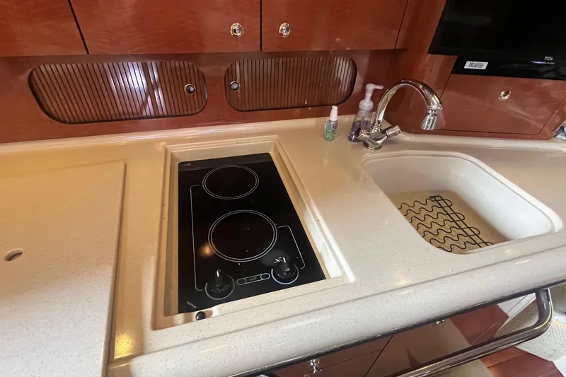 Slide: The Image of 2004 Sea Ray 340 Sundancer kitchen with stove, sink, and wooden cabinetry. - 25