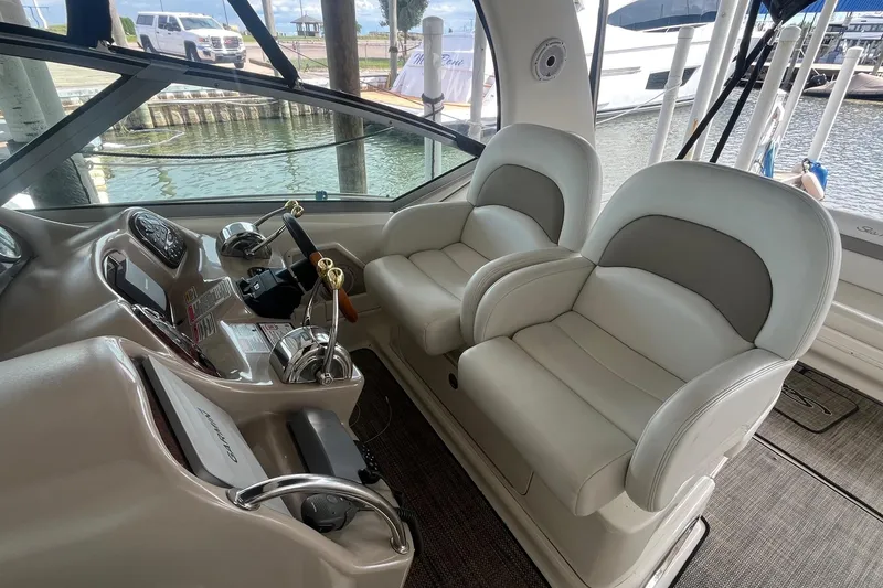 Slide: The Image of 2004 Sea Ray 340 Sundancer helm with dual seats and control panel, docked by the water. - 9