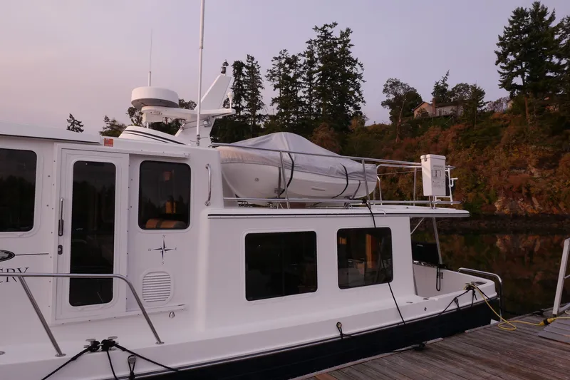 Slide: The Image of 2013 American Tug 395 docked, featuring a covered dinghy on the roof, surrounded by trees. - 8