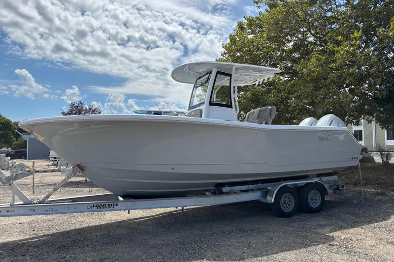 Slide: The Image of 2026 Sea Hunt Gamefish 25 boat on trailer, parked outdoors under a partly cloudy sky. - 11