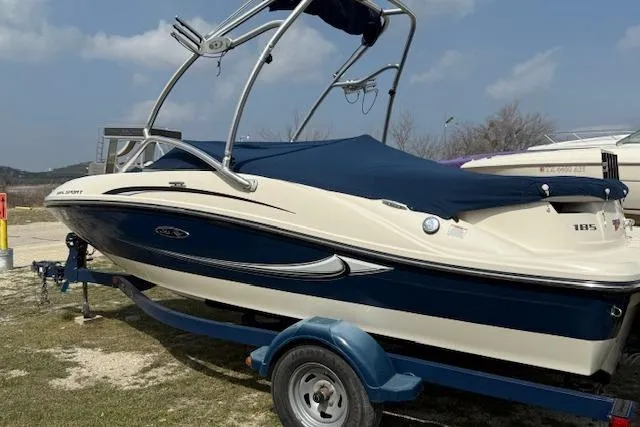 Slide: The Image of 2010 Sea Ray 185 Sport boat on trailer, blue and white design, parked outdoors. - 3