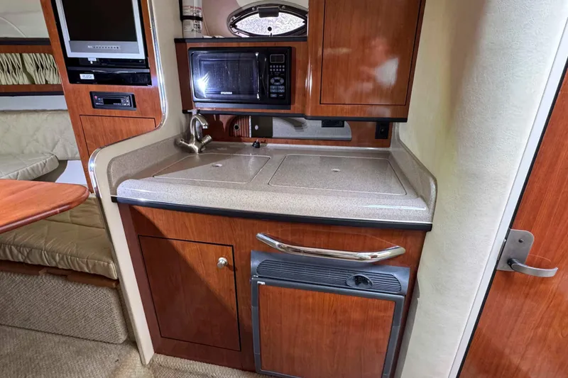 Slide: The Image of 2007 Sea Ray 280 Sundancer cabin kitchen with microwave, sink, and wood cabinetry. - 13
