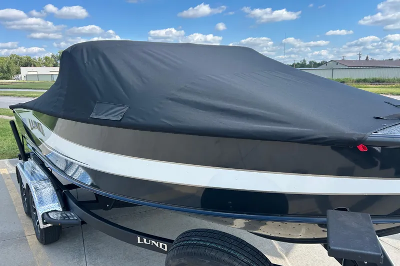 Slide: The Image of 2026 Lund 1875 Crossover XS boat with cover, parked outdoors under a blue sky. - 7