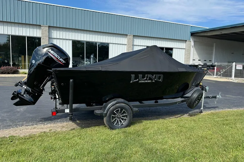 Slide: The Image of 2026 Lund 1650 Rebel XL Sport boat with cover on trailer, parked outside a building. - 27