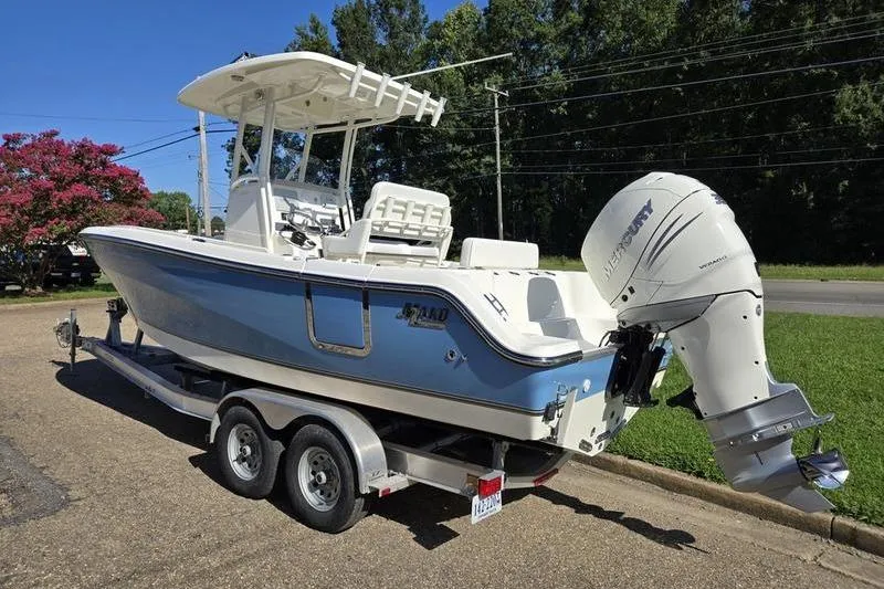 Slide: The Image of 2021 Mako 236 CC boat on trailer with Mercury outboard motor, parked outdoors. - 4