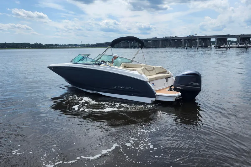 Slide: The Image of 2019 Regal 23 OBX boat cruising on a calm river with a bridge in the background. - 24