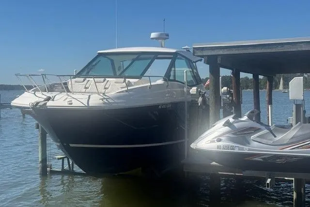Slide: The Image of 2023 Sea Ray Sundancer 320 Outboard docked beside a jet ski on a sunny day. - 2