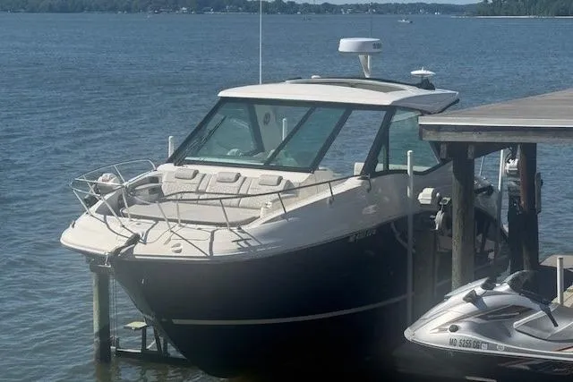 Slide: The Image of 2023 Sea Ray Sundancer 320 Outboard docked by the lake, with a jet ski nearby. - 3