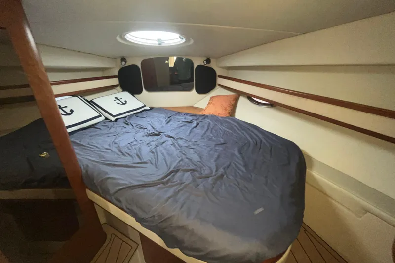 Slide: The Image of 2001 Cruisers Yachts 3470 Express cabin with bed, porthole, and nautical-themed pillows. - 13