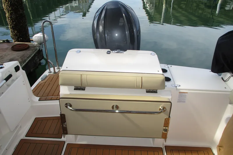 Slide: The Image of 2022 Ranger Tugs R-27 boat stern with seating and outboard motor, docked on calm water. - 34