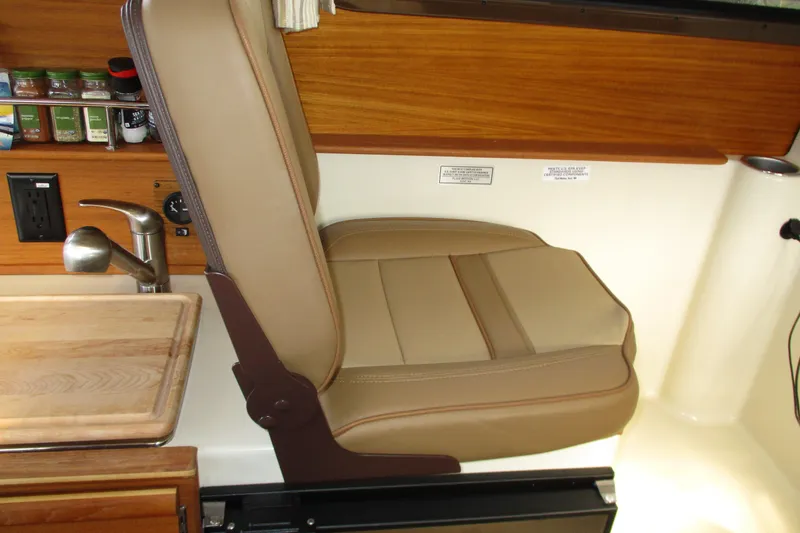 Slide: The Image of 2022 Ranger Tugs R-27 interior with beige seat, wooden accents, and compact kitchen area. - 45