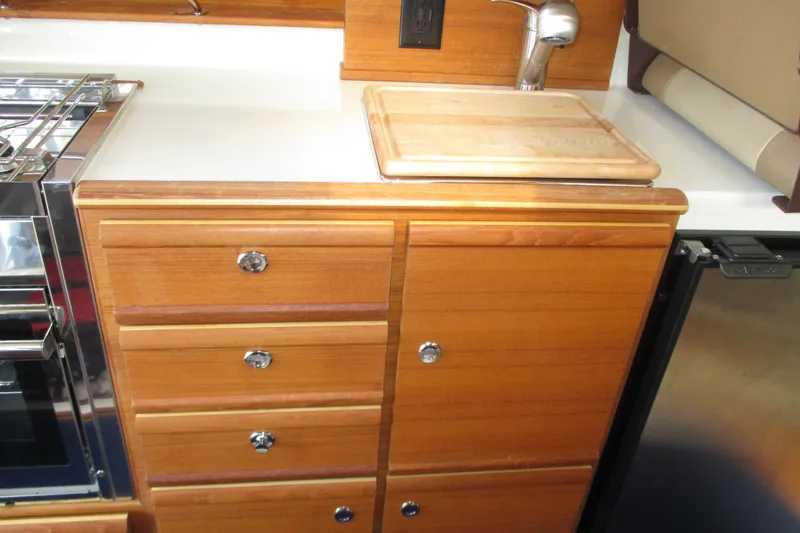 Slide: The Image of 2022 Ranger Tugs R-27 galley with wooden cabinetry, cutting board, and stainless steel appliances. - 48