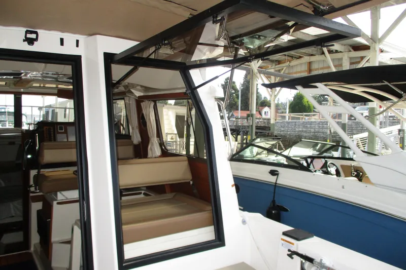 Slide: The Image of 2022 Ranger Tugs R-27 interior view with seating and open windows in a marina setting. - 64