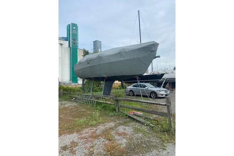 Slide: The Image of 1990 Tartan Thomas 35 sailboat covered and stored on land near a parked car. - 11