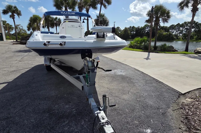 Slide: The Image of 2020 Tahoe 2150 CC boat on trailer, parked near palm trees and a lake. - 2