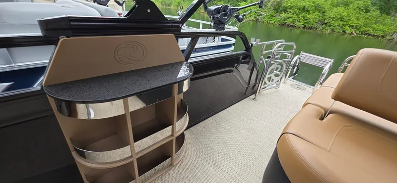 Slide: The Image of 2024 Regency 230 LE3 Sport boat interior with sleek seating and storage, near a serene lake. - 13