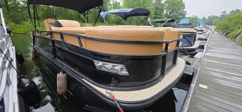 Slide: The Image of 2024 Regency 230 LE3 Sport pontoon boat docked, featuring tan seating and sleek black exterior. - 17