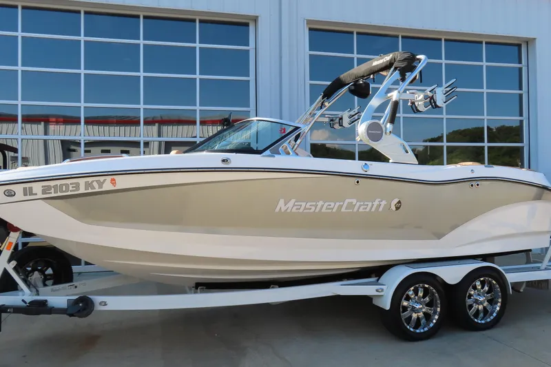 Slide: The Image of 2019 MasterCraft X22 boat on trailer, parked outside a building with large windows. - 1