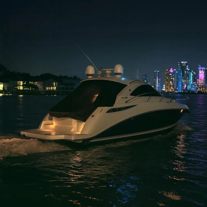 Slide: The Image of 2013 Sea Ray 410 Sundancer yacht cruising at night with city skyline backdrop. - 4
