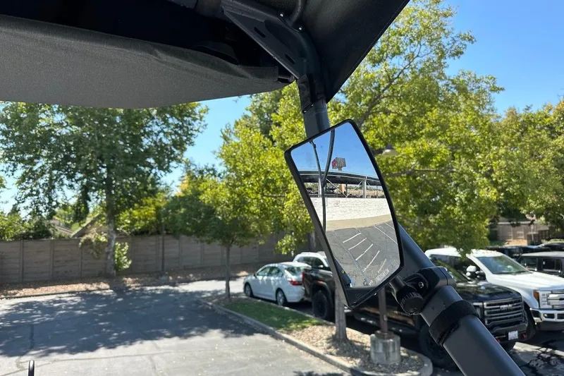 Slide: The Image of 2024 Sea-Doo Switch Sport 18 rearview mirror reflecting parking lot and trees. - 21