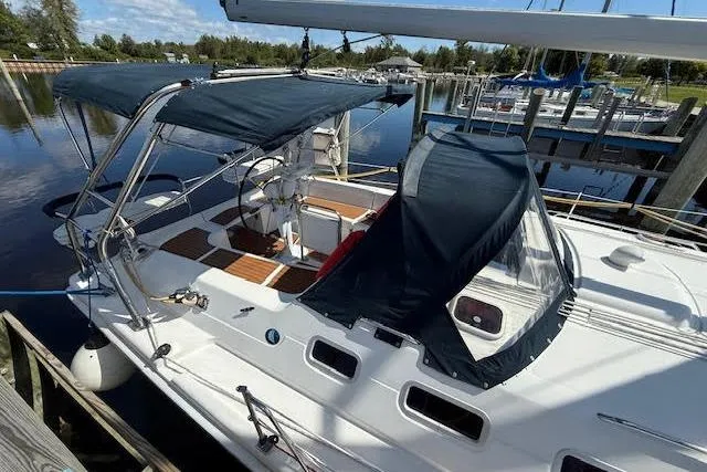 Slide: The Image of 2005 Hunter 38 sailboat docked, featuring a spacious deck and blue canopy. - 7