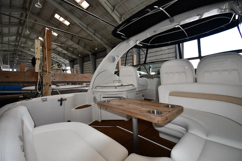 Slide: The Image of 2008 Sea Ray 340 Sundancer interior with white seating and wooden table in a boatyard. - 20