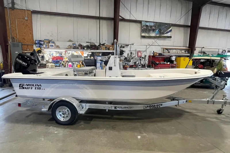 The Image of 2026 Carolina Skiff E18 JVX CC boat on trailer in a workshop setting. - 1
