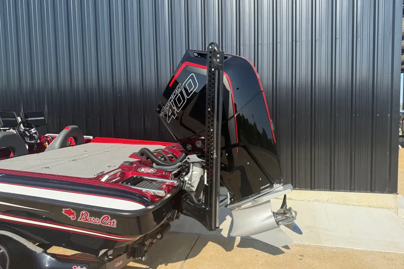 Slide: The Image of 2023 Bass Cat Jaguar STS boat with powerful outboard motor, parked near a metal wall. - 14