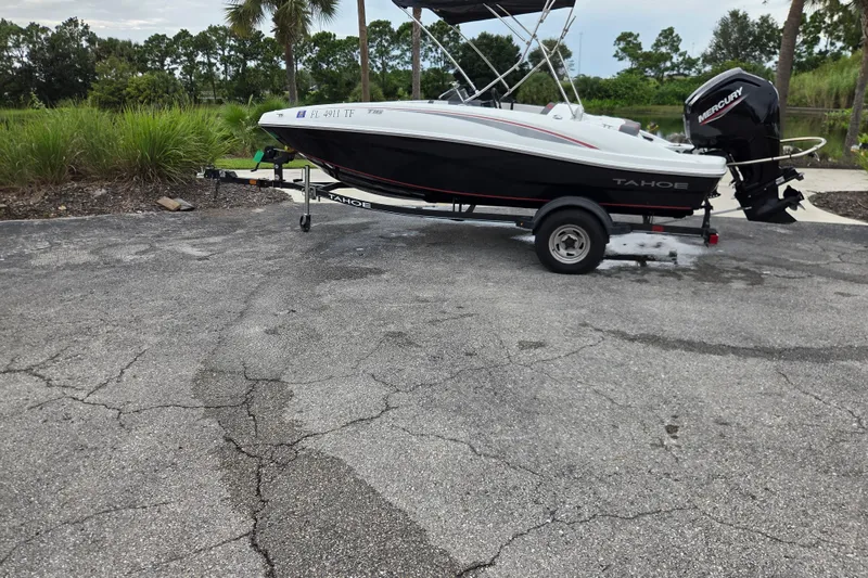 The Image of 2022 Tahoe T16 boat on trailer with Mercury outboard motor, parked on cracked pavement. - 0