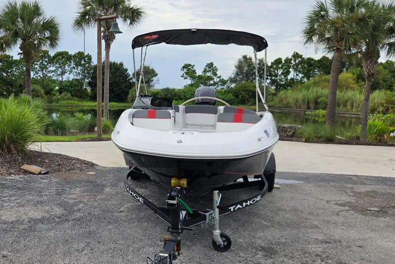 Slide: The Image of 2022 Tahoe T16 boat on trailer, parked near lush greenery and palm trees. - 2